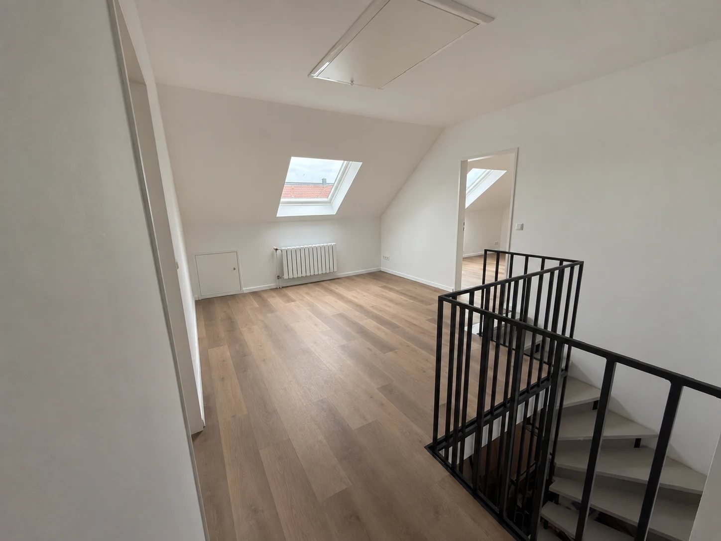 Heller Raum unter dem Dach mit neuem Boden, Dachfenster und schwarzem Treppengeländer